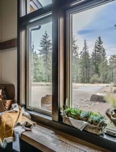 Photo of a brown-framed casement window inside a home with view of pine trees outside